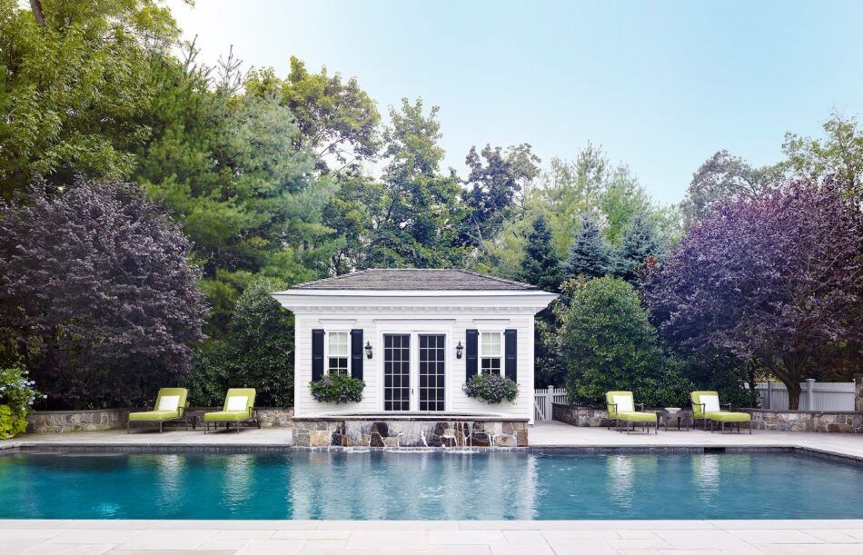 Un pool house blanc décoré par Douglas Graneto, avec des chaises longues vertes