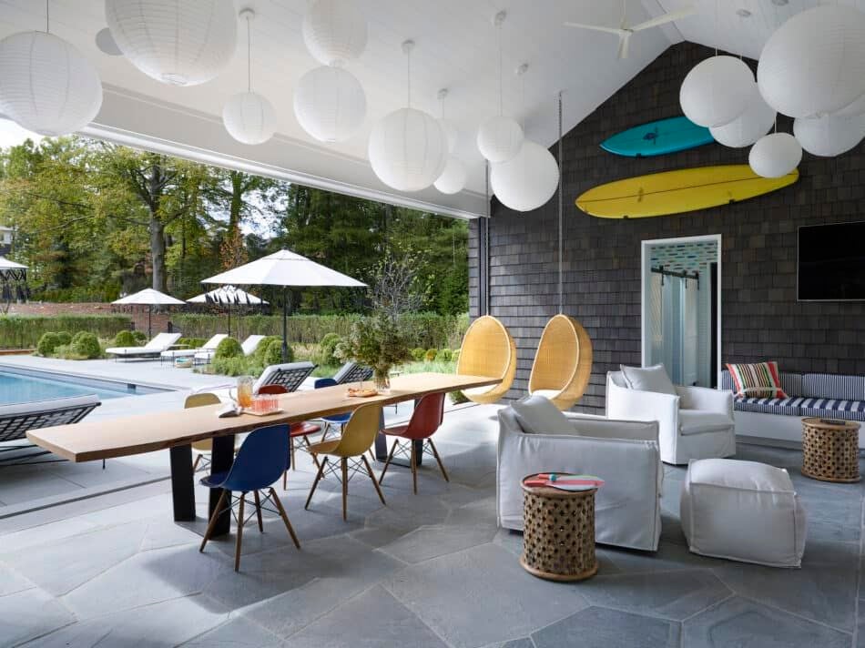 Un pool house à l'intérieur décoré par Fawn Galli, avec des chaises coquilles colorées d'Eames