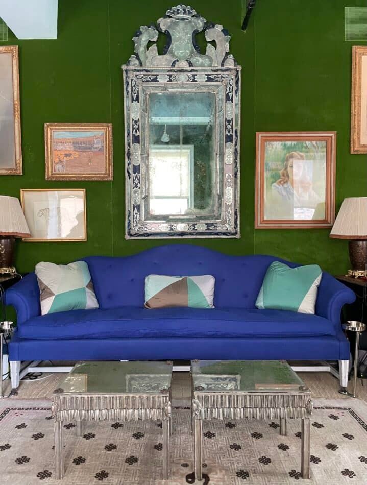 Un miroir vénitien accroché au-dessus d'un canapé bleu sur un mur vert dans le bureau de Miles Redd