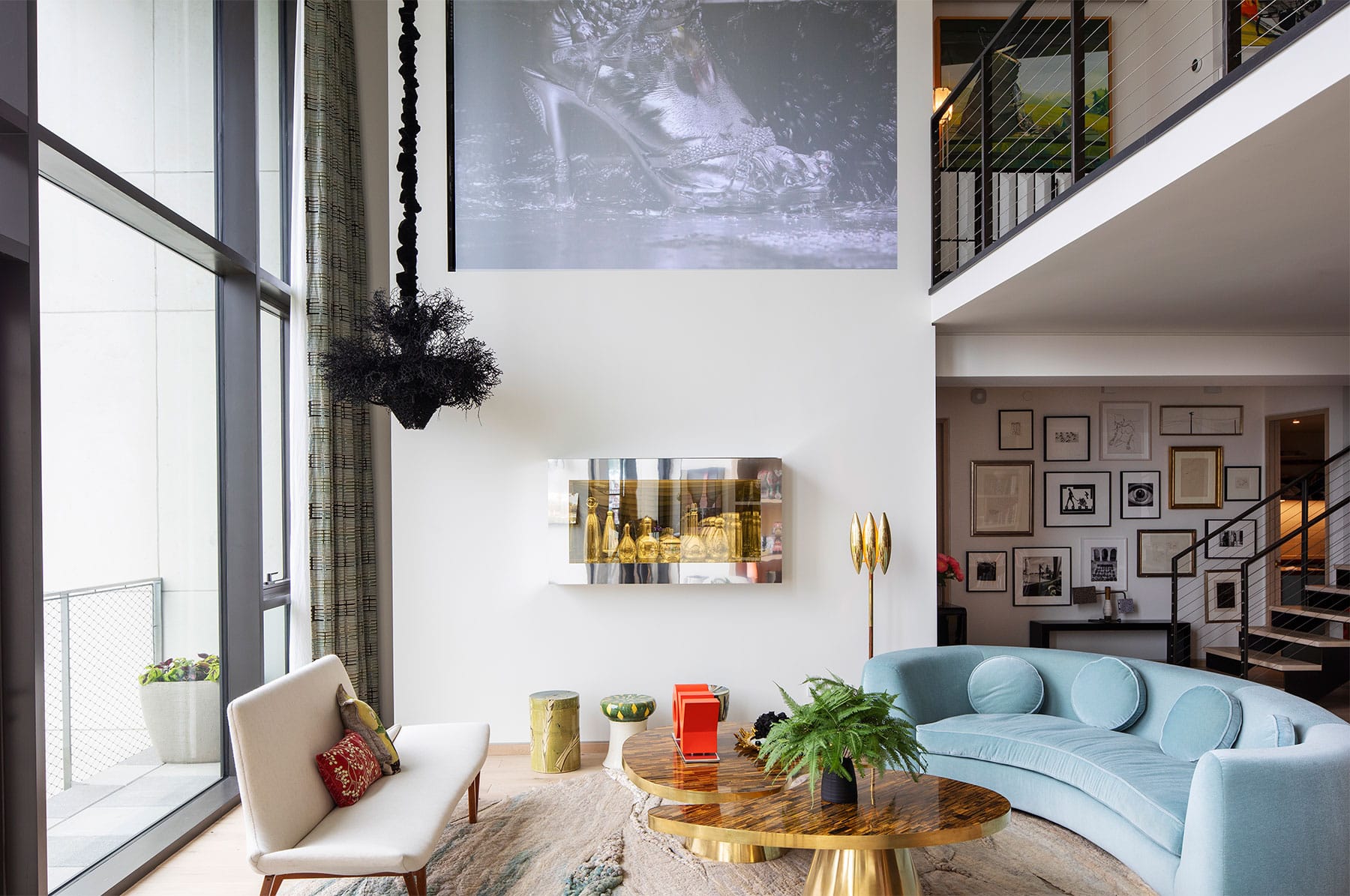 Marilyn Minter video installation is projected on the wall of the living room above a Josiah McEleheny vitrine and 1940s ceramic stools from 1stdibs. The black hanging sculpture is by Petah Clyne, and the sofa is by India Mahdavi
