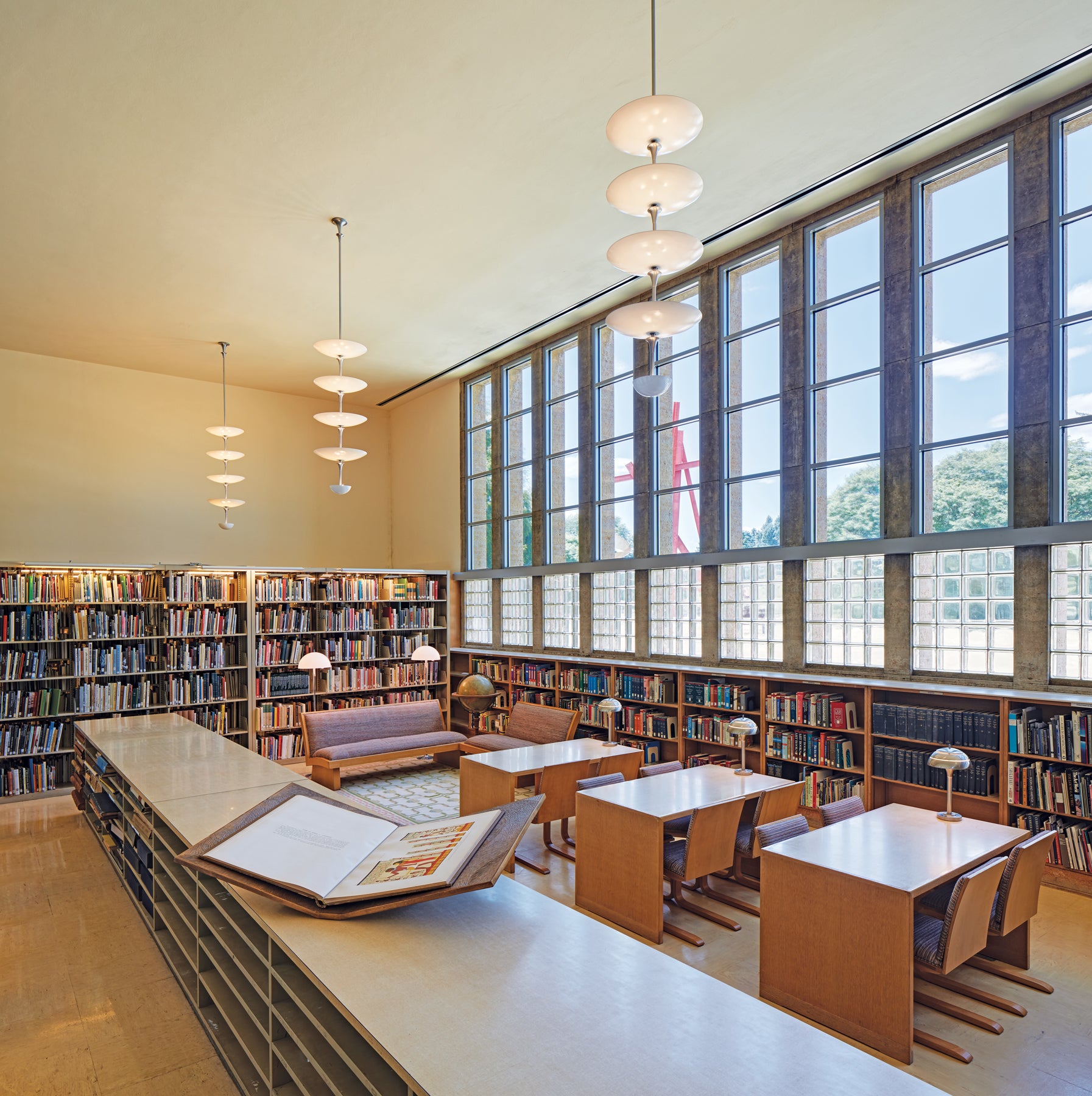 Intérieur de la bibliothèque de la Cranbrook Academy of Art, avec luminaires à plusieurs niveaux et étagères de livres.