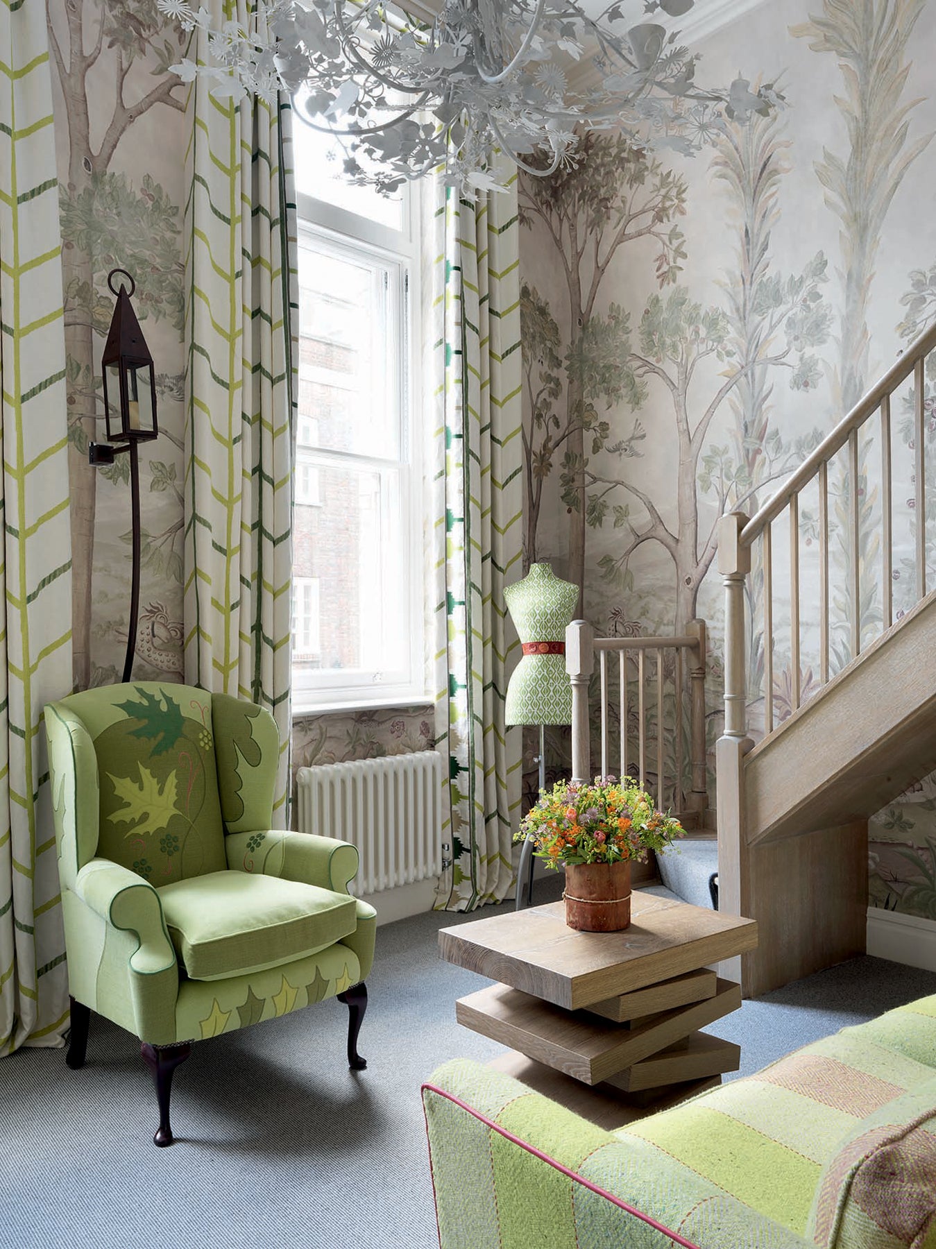 Section d'un salon avec un papier peint comportant des arbres comme motif, un fauteuil vert, un mannequin de couture et un canapé