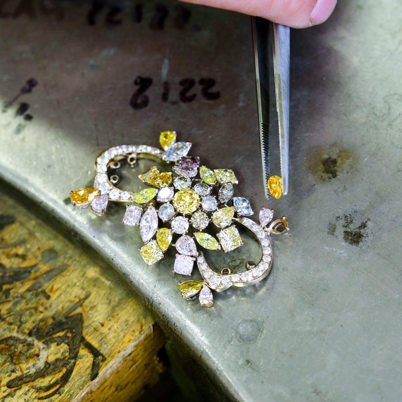  À gauche : bague cocktail, diamant en forme de cœur brun-orangé chic 7,08 carats certifié GIA, 2010. À droite : un artisan en train de sertir une pierre sur une broche colorée.