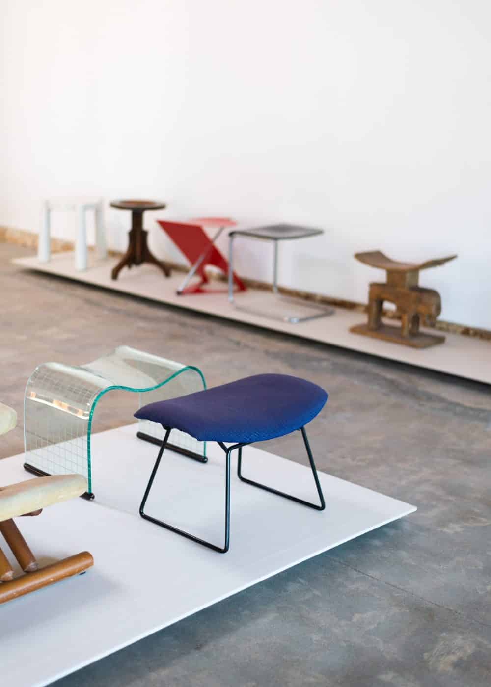 Tabouret Onda Incisa de Vittorio Livi, en verre incurvé et datant de 1973, à côté d'une ottomane Bird d'Harry Bertoia, recouverte d'un tissu bleu