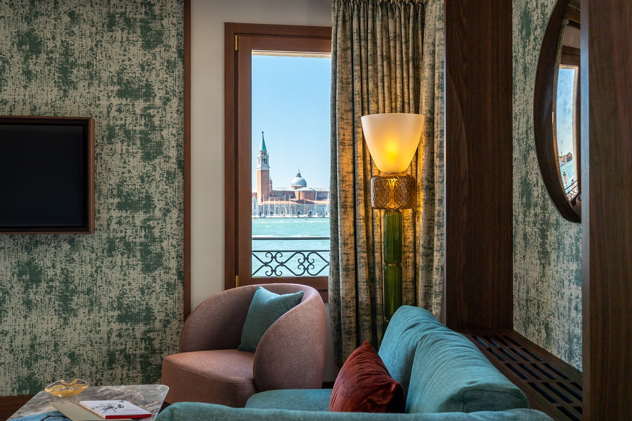 Gästezimmer im neuen Hotel Ca' di Dio in Venedig mit maßgefertigten Betten, Sesseln, Sofas und kleinen Tischen, die Patricia Urquiola zusammen mit Molteni entworfen hat, und Blick durch das Fenster auf das Kloster San Giorgio Maggiore auf der anderen Seite des Canal Grande
