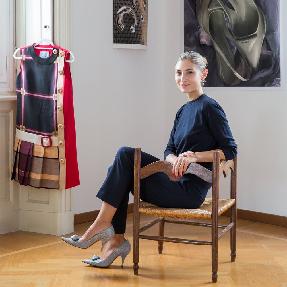 Jenny Walton seated in a late-20th-century French corner chair next to a vintage plaid Prada minidress hanging from a window shutter