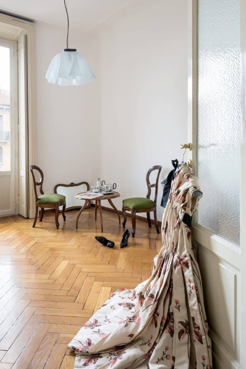 Jenny Waltons Mailänder Wohnung mit einem cremefarbenen Prada-Kleid mit rosa Blumen, das an einer Türklinke hängt, einem holzgerahmten Spiegel aus den 1960er-Jahren, der an der Wand lehnt, zwei barocken italienischen Stühlen mit grünen Polstern und einem Cocktailtisch von Osvaldo Borsani, auf dem ein silbernes Tablett steht 