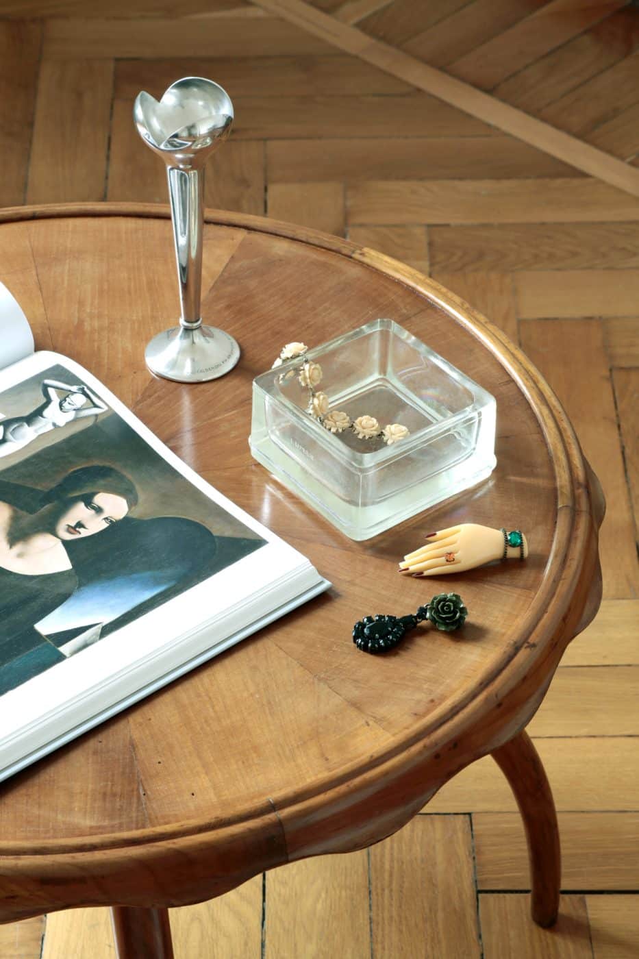 Cocktailtisch von Osvaldo Borsani in der Mailänder Wohnung von Jenny Walton; darauf ein aufgeschlagenes Kunstbuch, eine schlanke silberbeschichtete Vase, ein eckiger Aschenbecher aus Glas und Vintage-Schmuck